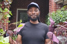 Marcus Bridgewater is smiling at the camera while holding plants in both of his hands.