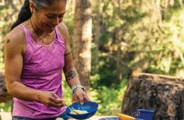 Maria Hines is cooking outside. She's wearing a pink tanktop and smiling down at the food she's preparing.