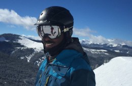 Mike Carey in helmet and goggles in front of snowy backdrop.