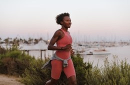 Iman running in a bright workout outfit along a dirt road next to water