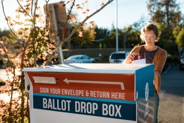 A woman slips her ballot into a ballot drop box