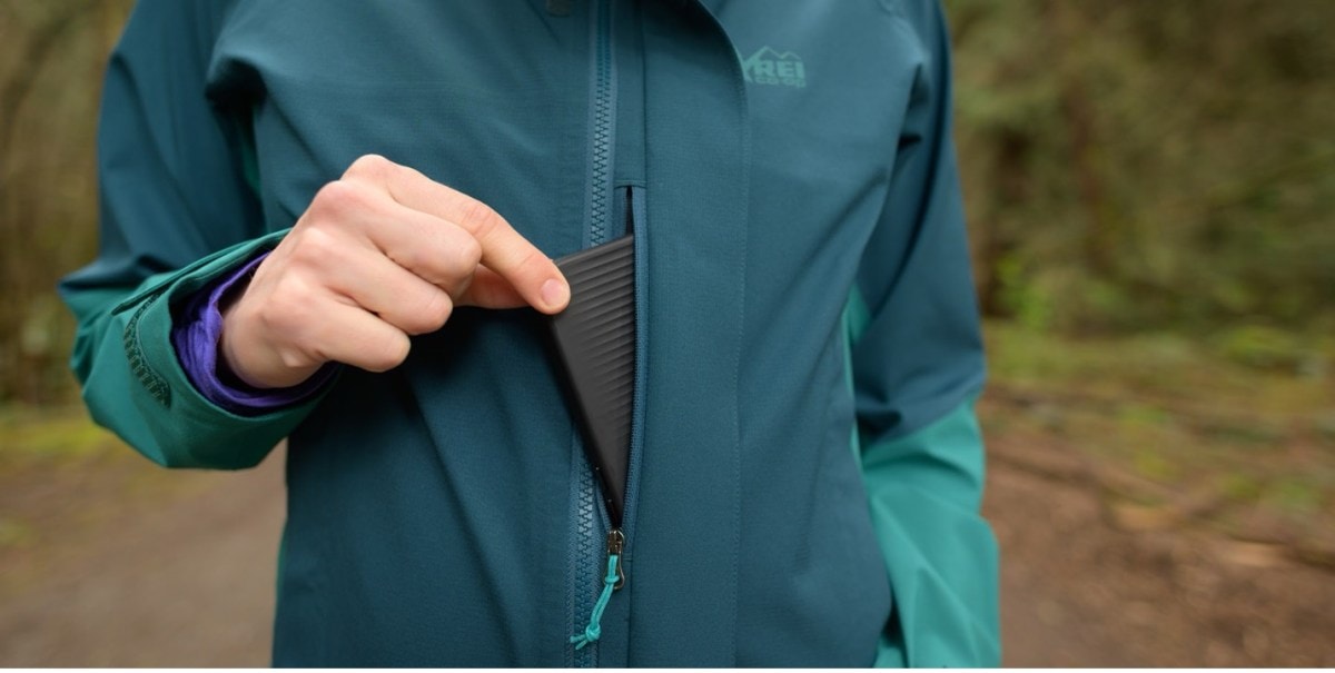 Detail of the chest pocket on the Flash Stretch rain jacket. The model is pulling an iPhone in a black case out of the pocket.