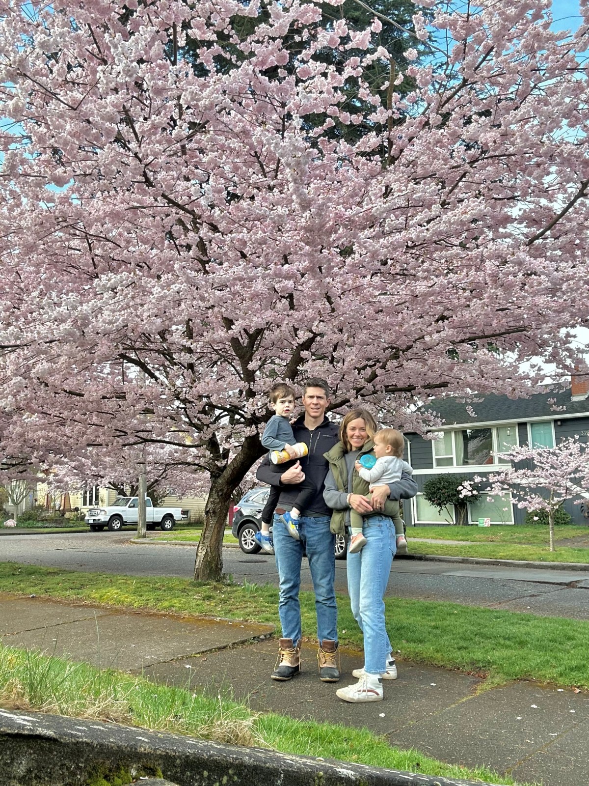 A family stands in front of a large cherry tree in full blossom.