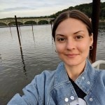 A selfie of a smiling person in a denim top in front of a body of water.