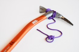 A close-up of an ice axe with an orange handle on a white background