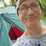 A person wearing a hat takes a selfie in front of an REI Co-op tent