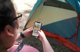 A camper standing in front of a tent uses the Fridie Outdoors app.