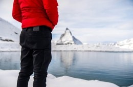 A person wearing DUER jeans, visible from behind from the waist down looks out over a glacial lake.