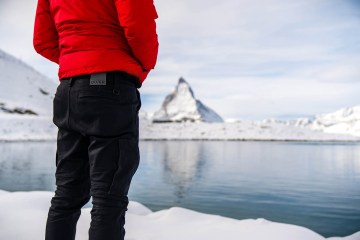 A person wearing DUER jeans, visible from behind from the waist down looks out over a glacial lake.