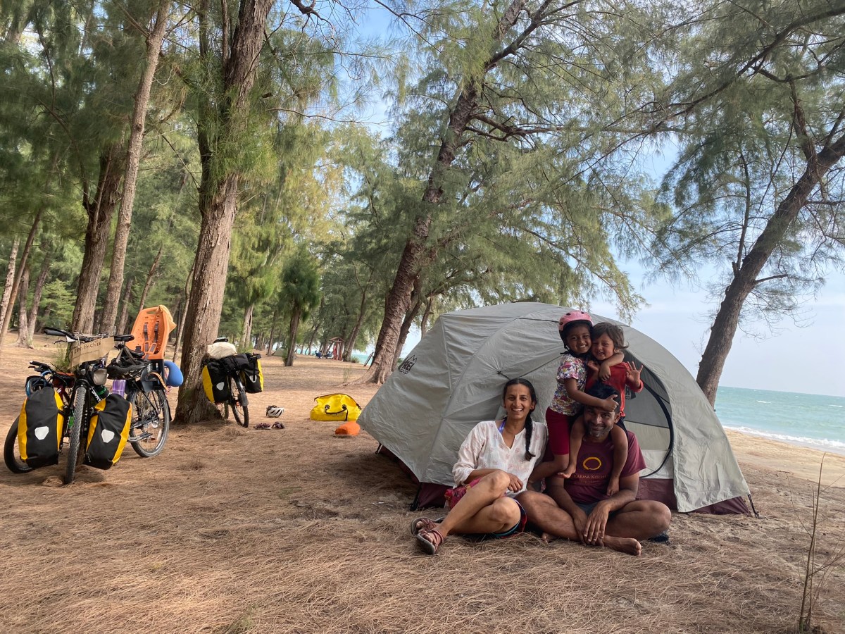 Photo of two adults and their two children sitting on a beach near their Half Dome tent.