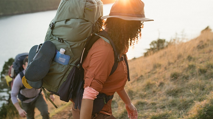 A backpacker wearing the REI Co-op Traverse 60 scales a grassy hill.