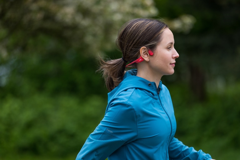 A woman runs in a pair of red OpenRun Shokz Headphones