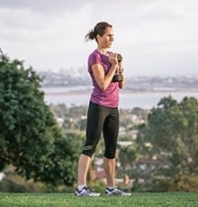 Woman standing holding a dumbbell vertically in front of chest