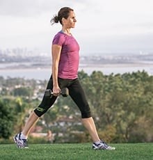 Woman standing with one foot stepped forward and dumbbells in hands