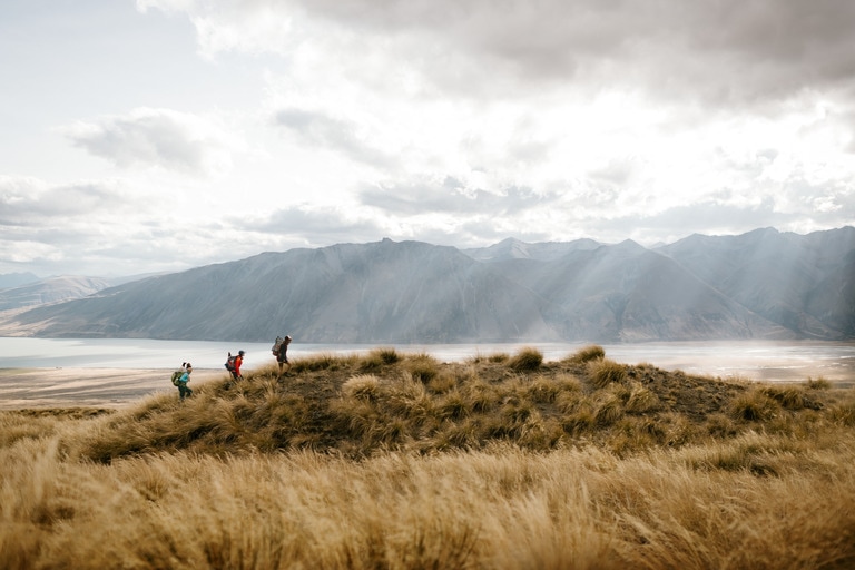 Three people hiking up a hill overlooking a valley.