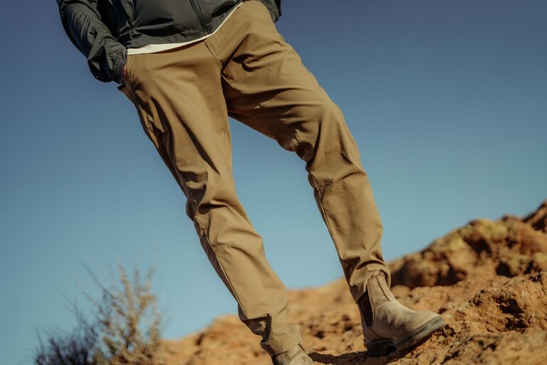 A person stands on a rocky ridge with their hands in the pockets of their KUHL hiking pants.