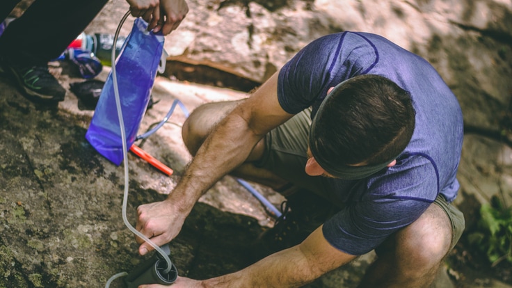 A backpacker filters water at a stream.