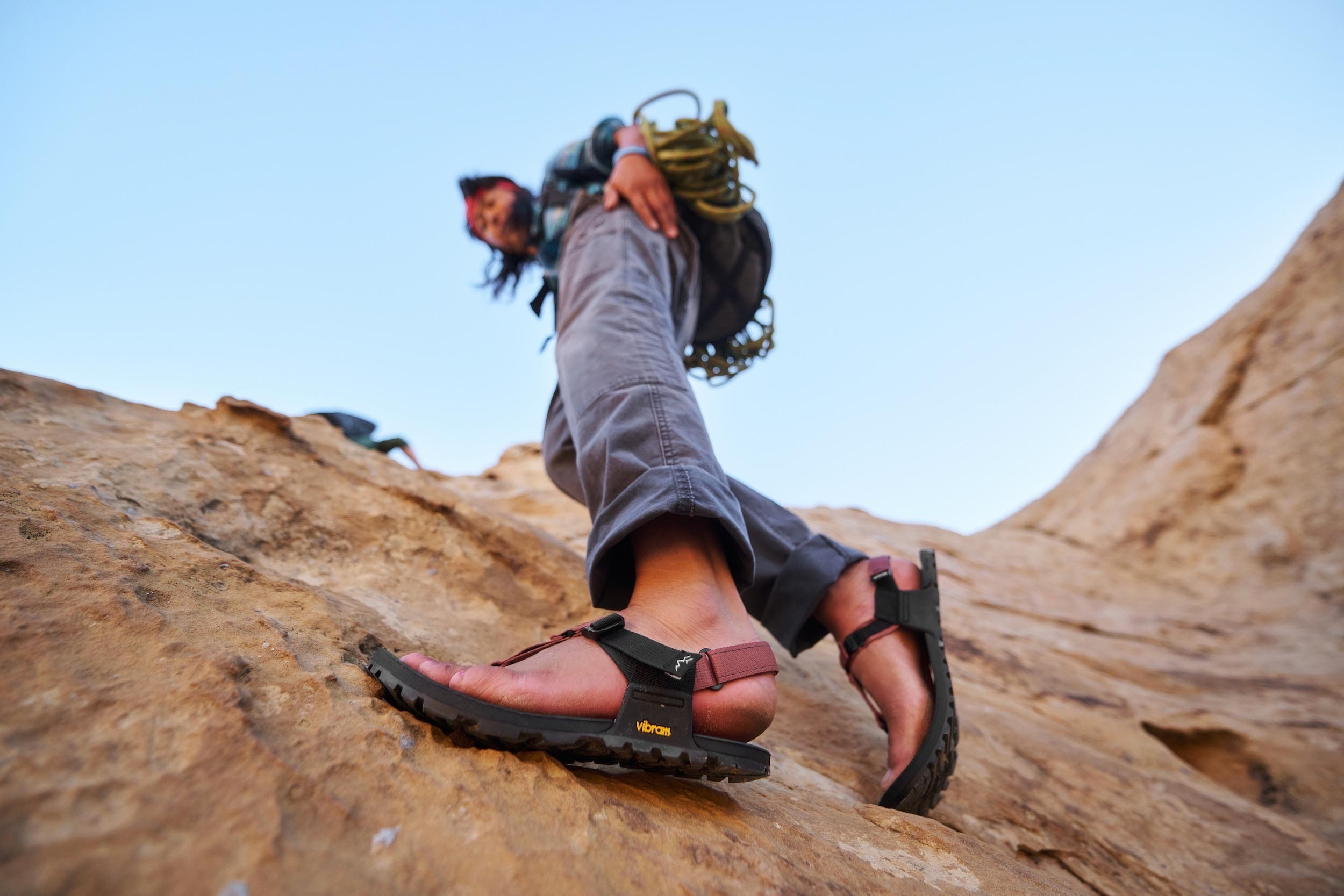 A hiker wearing Bedrock Cairn Evo sandals climbs up a rocky outcropping.