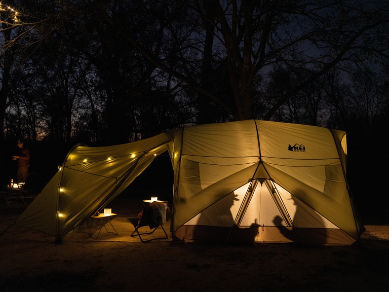 Two people sit inside a lit tent at night.