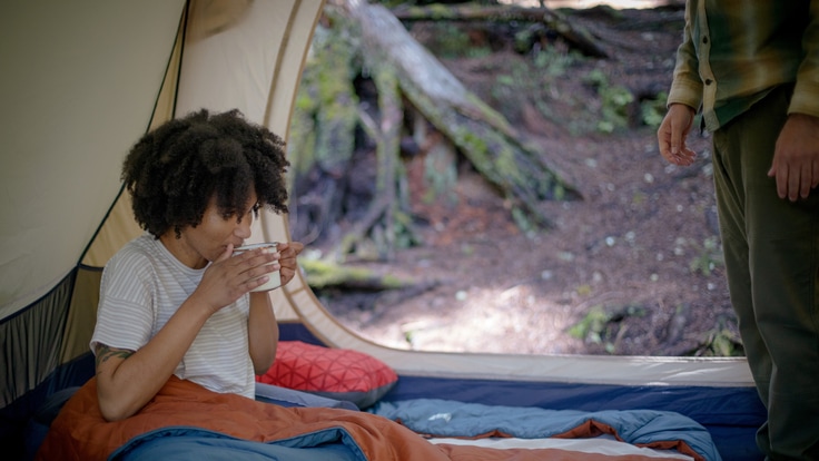 A woman drinks coffee from inside her tent.