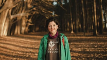 A hiker stands facing the camera on a tree-lined path