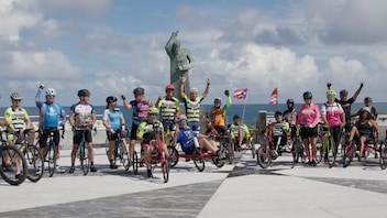 A group of adaptive athletes on bikes pose in a plaza overlooking a body of water.