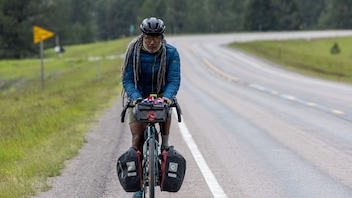 A bikepacker rides on the shoulder of a paved road with trees in the background