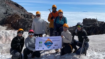 A group of seven indigenous climbers wearing cold-weather climbing gear stand on the summit of Tahoma.