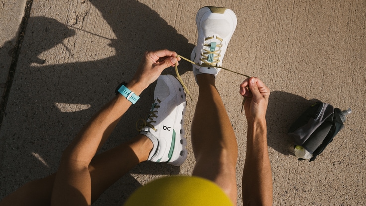 A person sitting down laces up a pair of On Cloud 5 shoes.