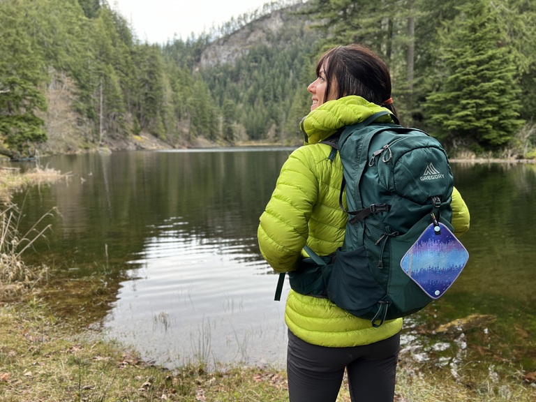 A hiker stands in front of a body of water with their back and backpack turned to the camera.