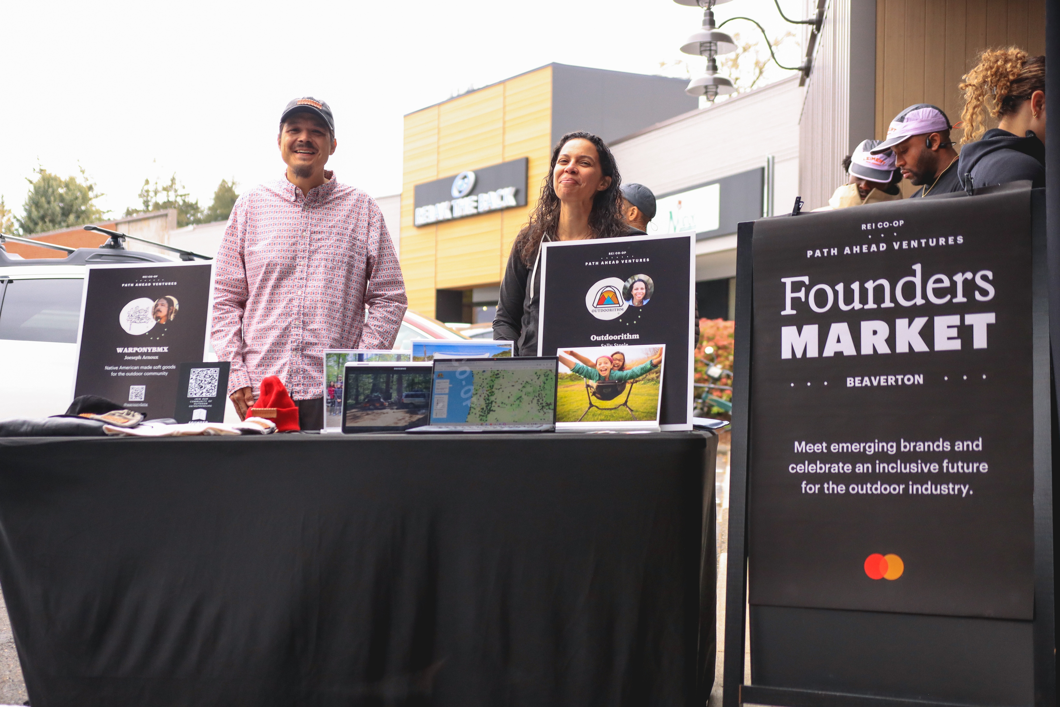 Two people stand behind a booth to speak to customers about their businesses.