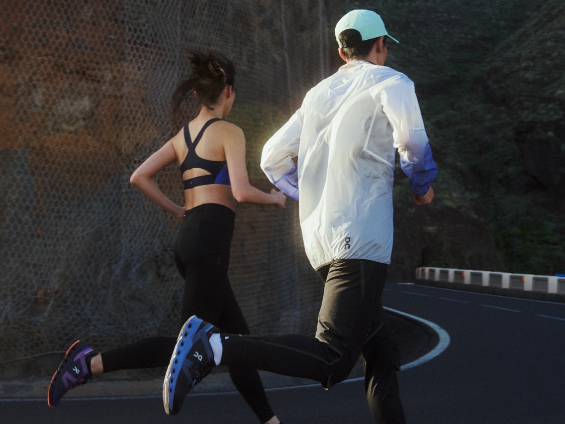 Two runners wearing On and jogging uphill on a mountain road.