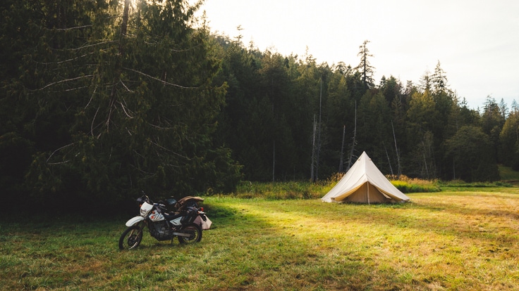 Grassy campground with a tent in the background and a motorcycle in the foreground.