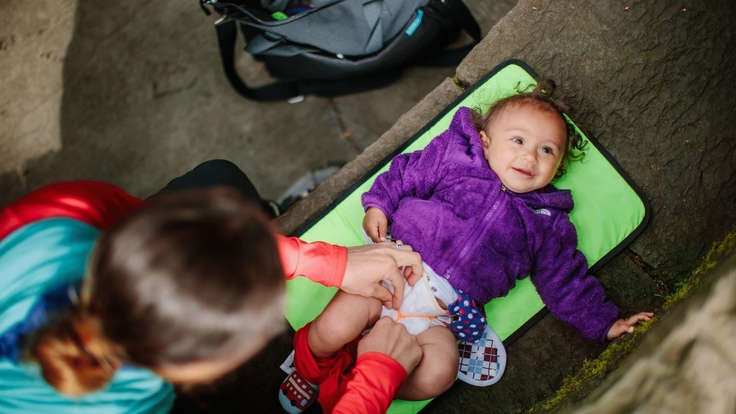 A person changes the diaper on a baby on lies on a green mat.