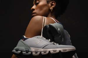 A woman poses with running shoes hanging over her shoulder.