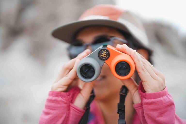 A person looks through a pair of gray and orange binoculars