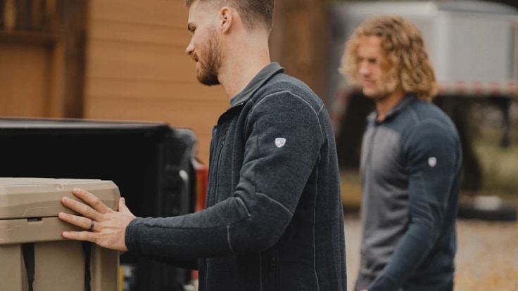 Two people wearing fleece jackets load up a flatbed truck.