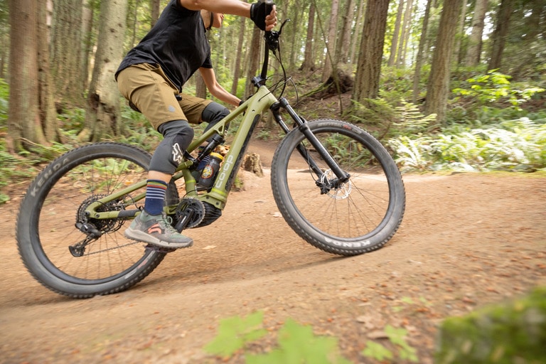 A person rides an electric mountain bike on a dirt trail in the forest.