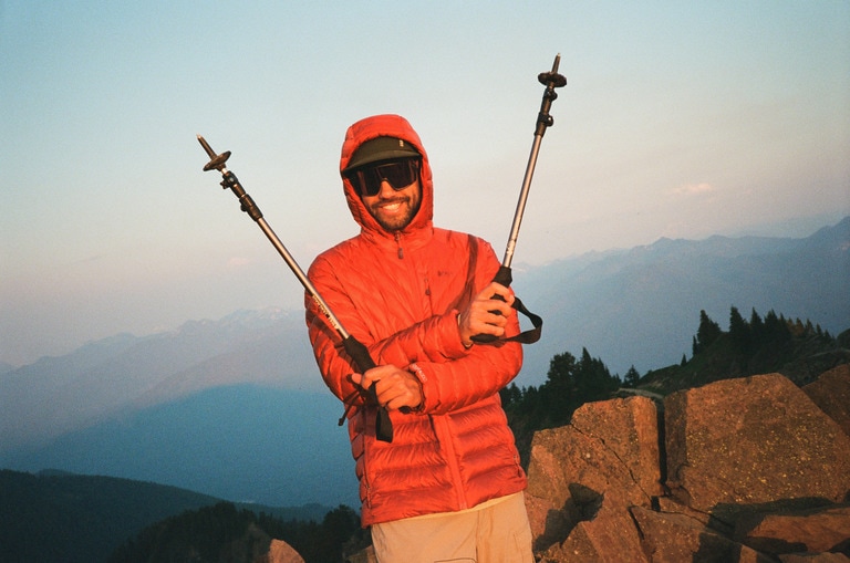 A person standing on a ridge holds up two collapsed trekking poles