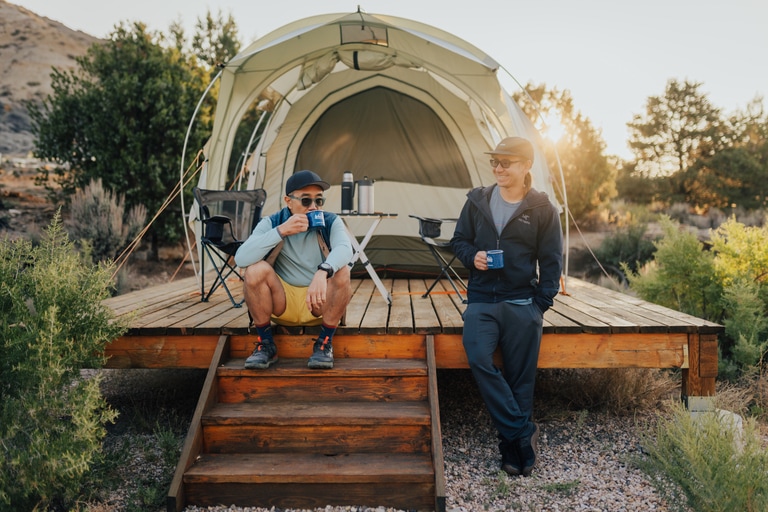 a pair of campers drink coffee next to a tent