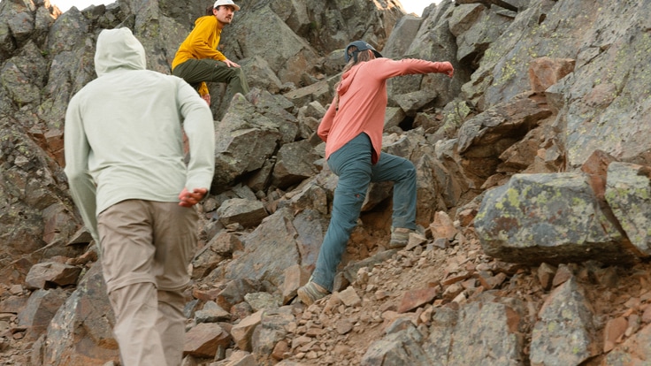 Three hikers scramble up a boulder-strewn hillside