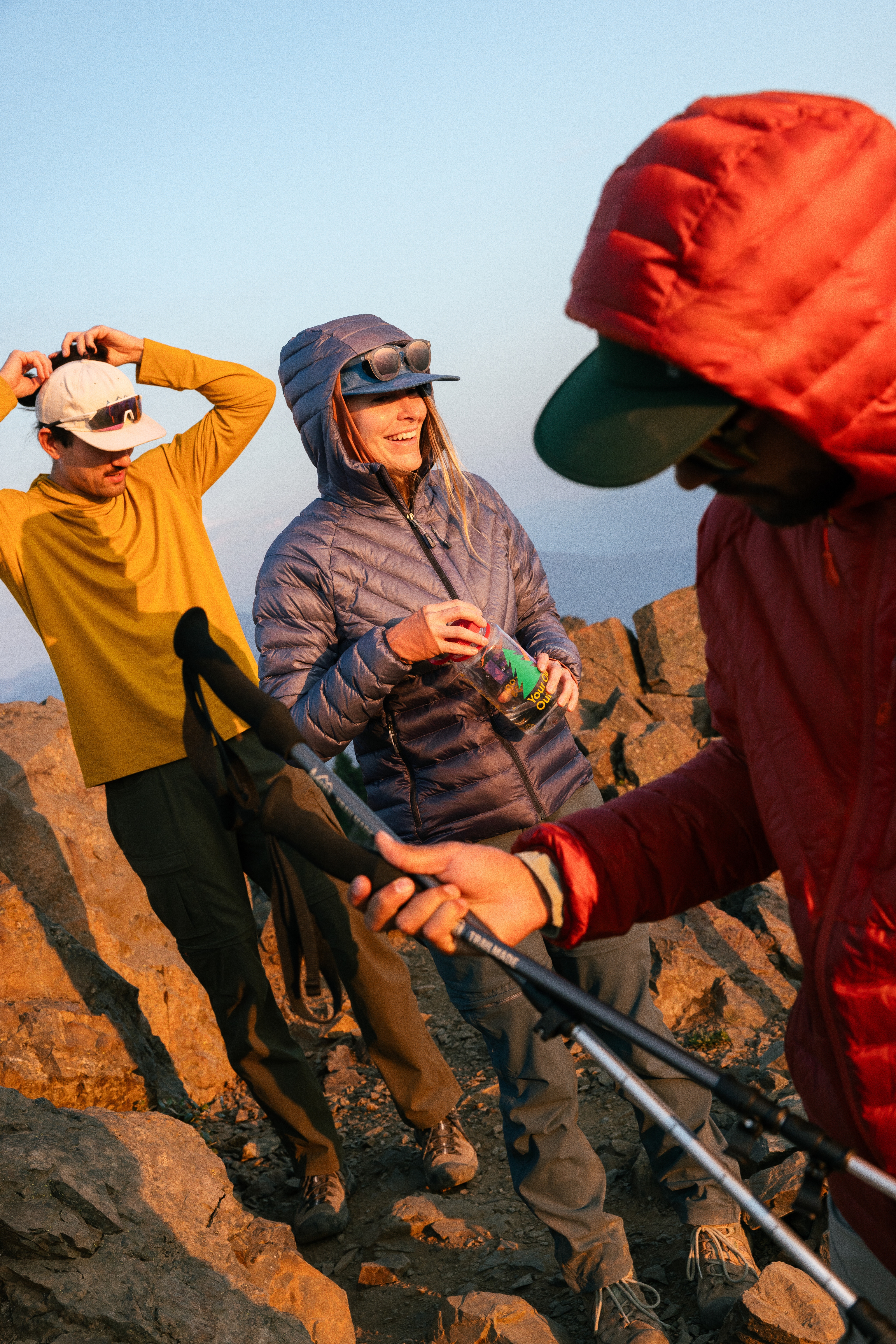 Three hikers in R E I Co-op brand gear take a break on a summit trail.