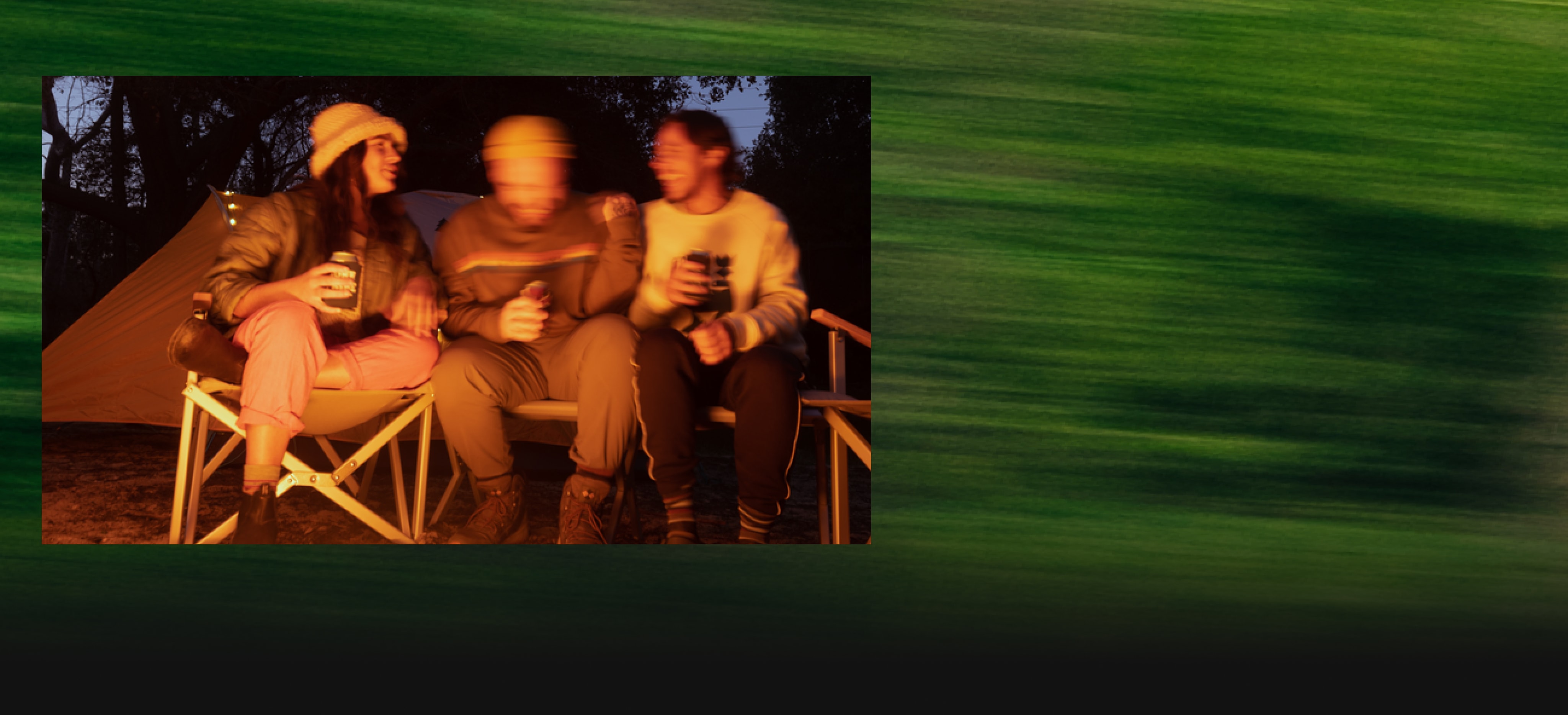 A group of friends having a laugh with drinks over a campfire.