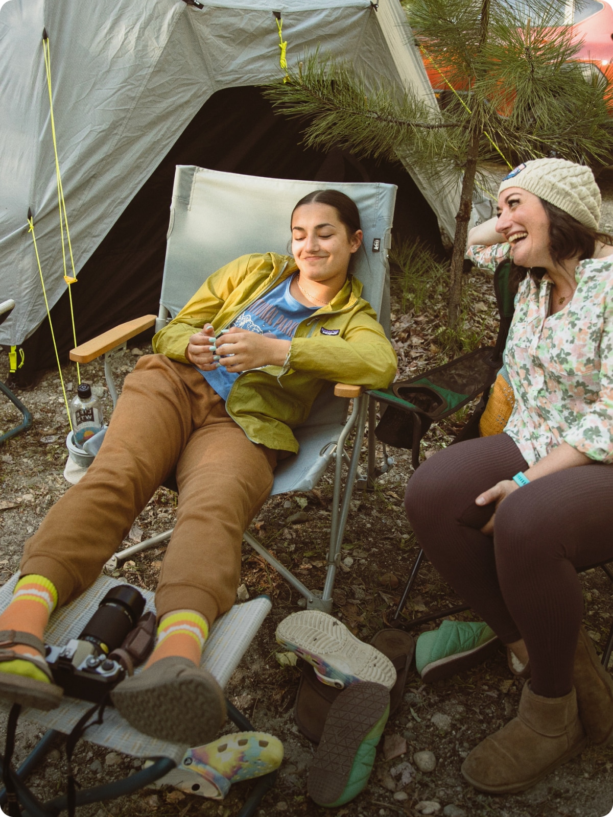 Two people relaxing on chairs in front of their campsite.