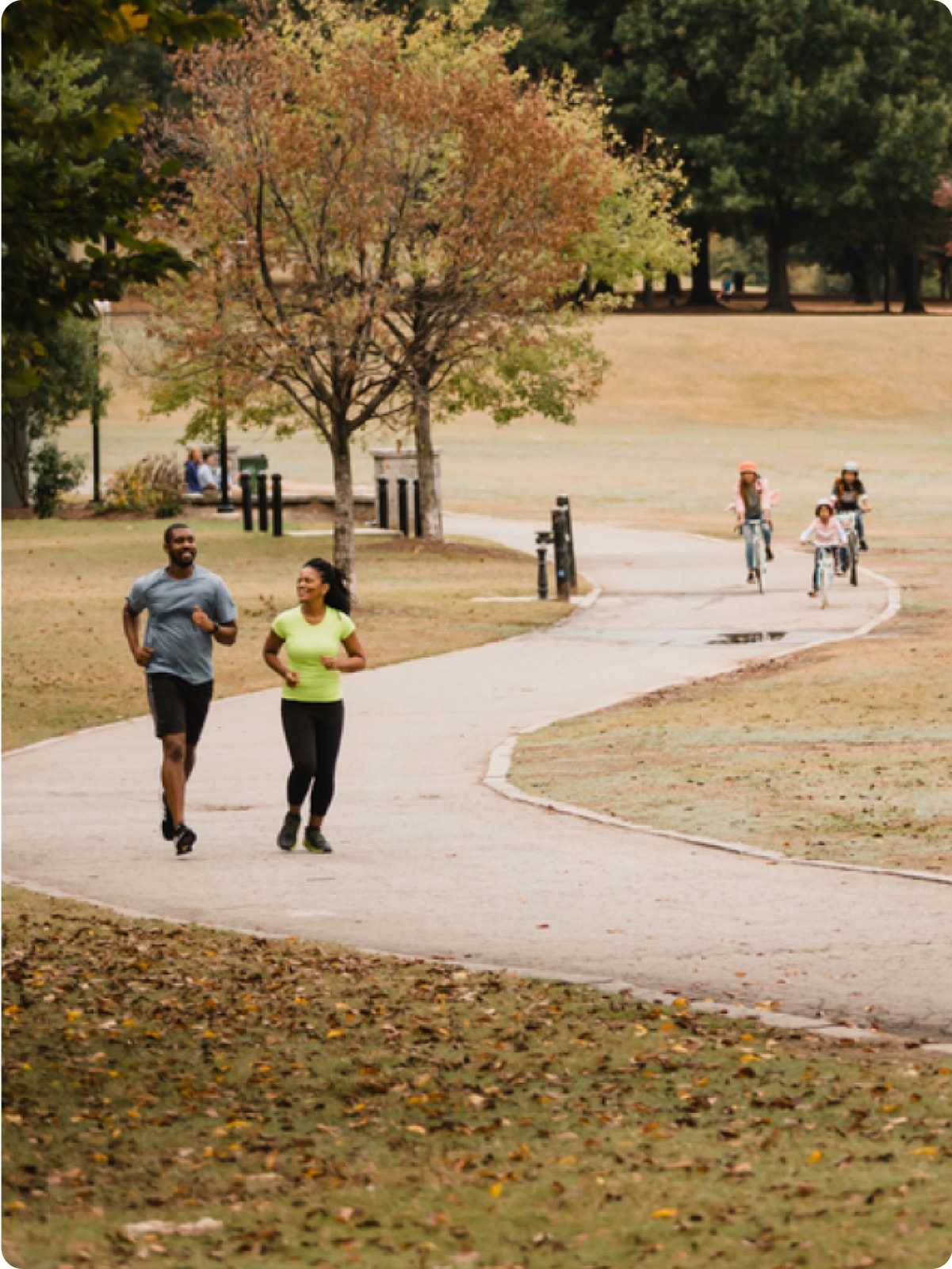 Adults running, children biking at a park.