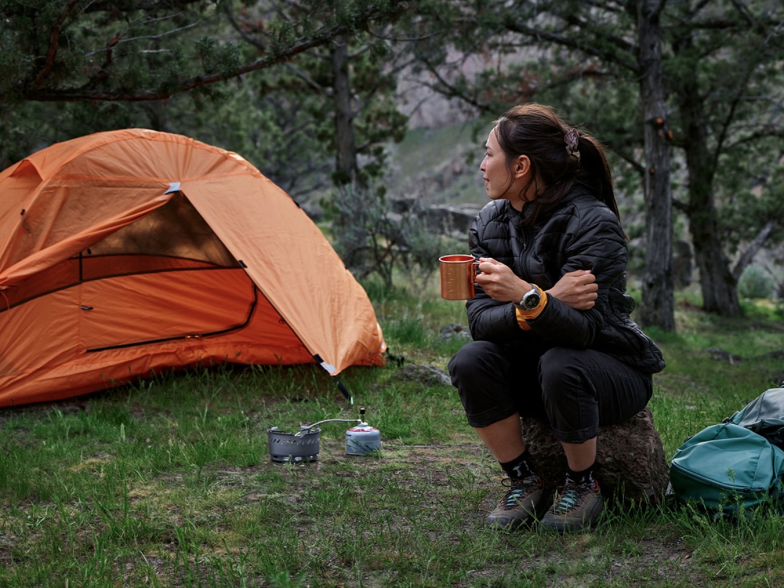 A person sitting at their campsite holding a mug.