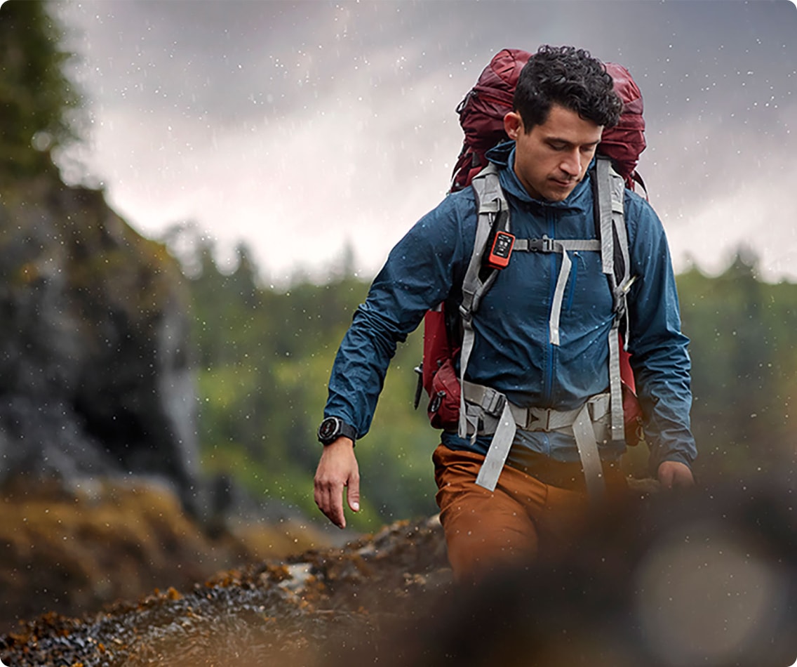 Person hiking in the rain with a Garmin sport watch and inReach® satellite communicator.