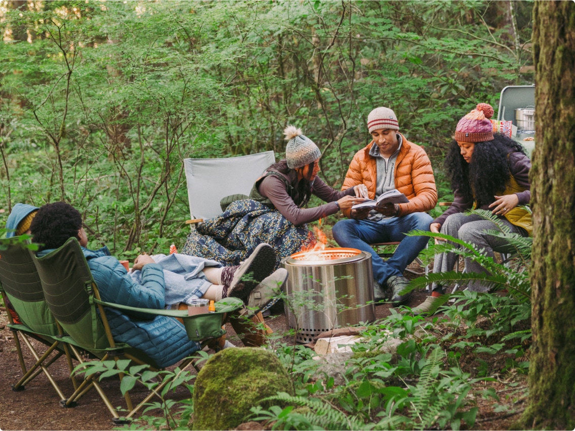 A group of friends staying warm around a campfire in the forest. 