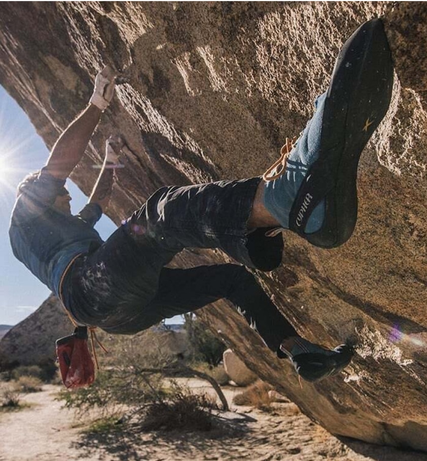 A climber bouldering in the desert with a crash pad ready below.