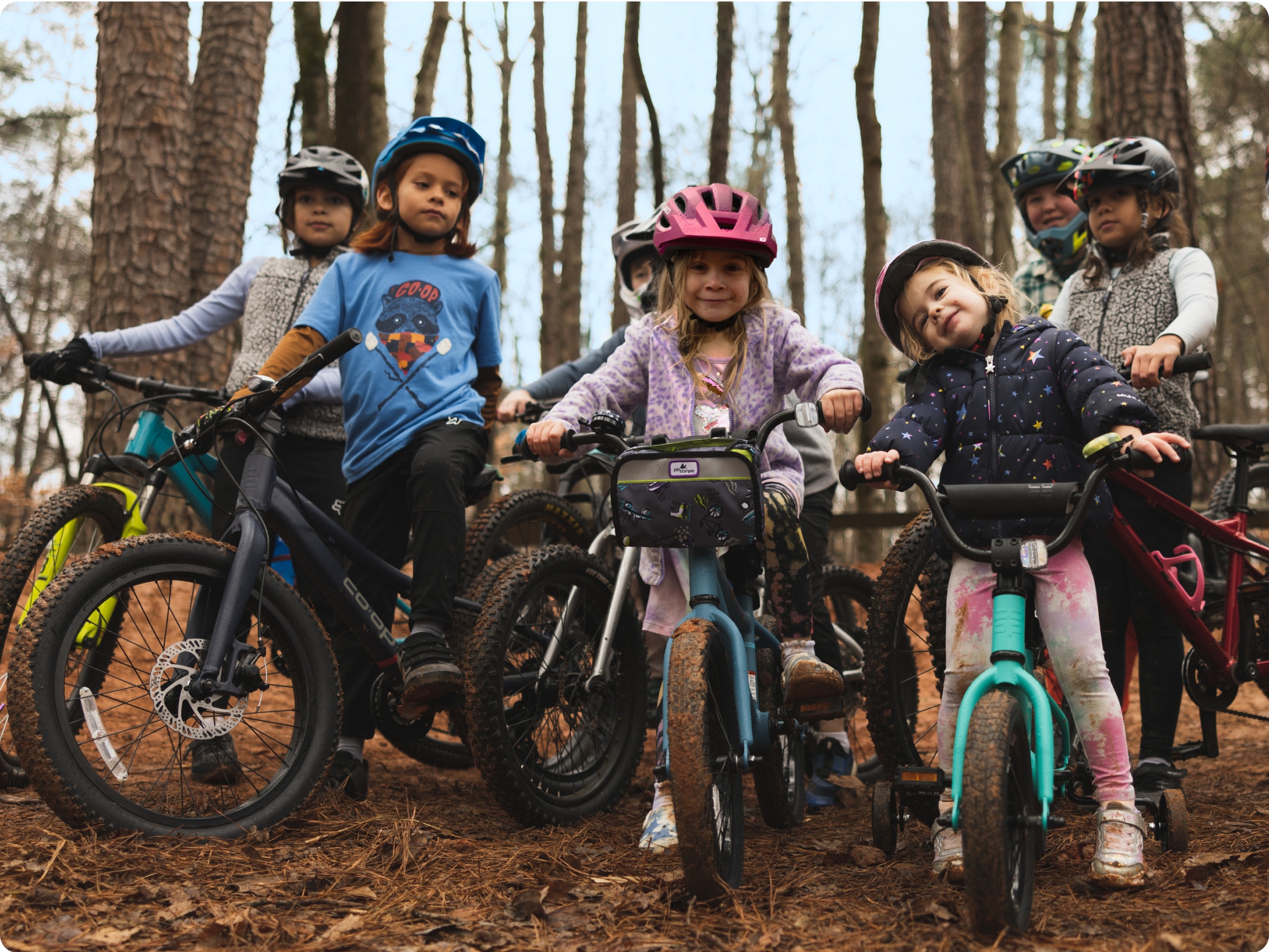 A group of children ride bikes on a wooded path.